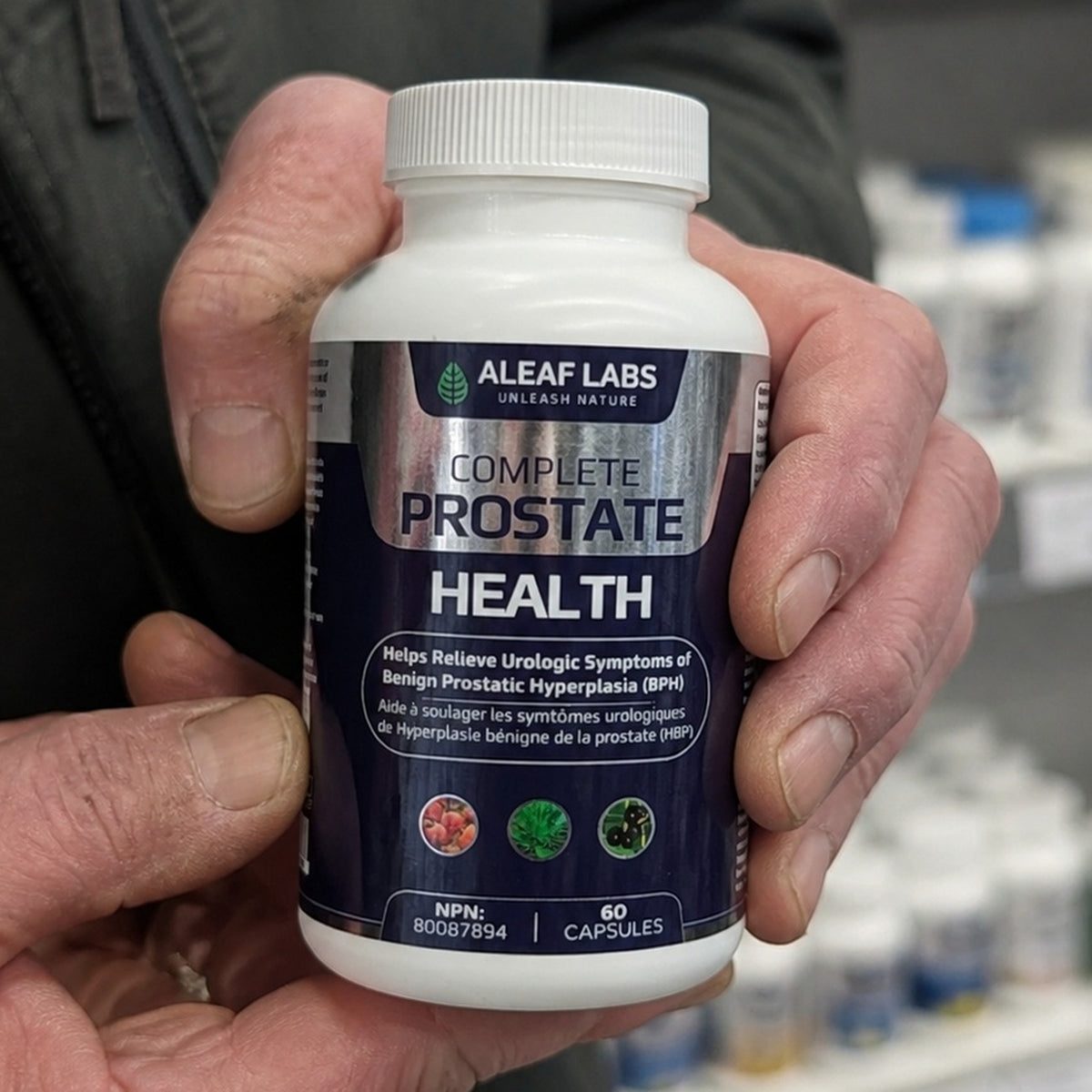 A man's hand holding a bottle of Complete Prostate Health, front label showing NPN 80087894 and the licensed claim